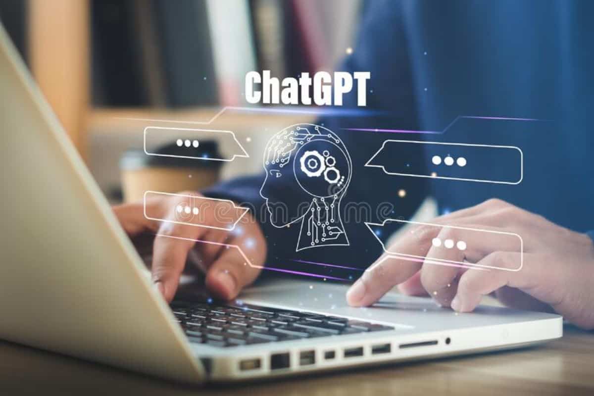 Close-up image of a hand typing on a laptop keyboard with a 'ChatGPT' and robot hologram around it